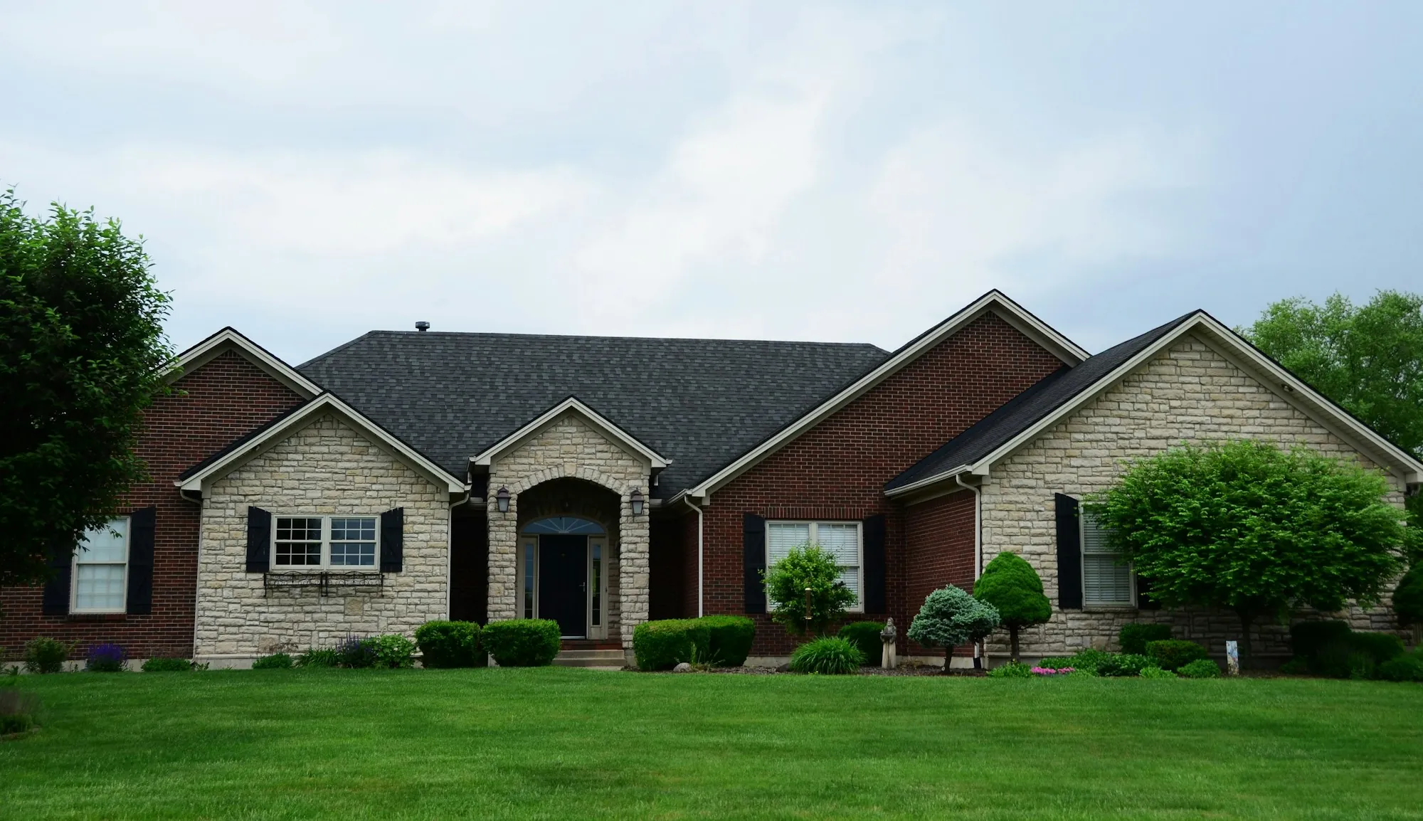 Brick and stone ranch house with trimmed shrubs along the front